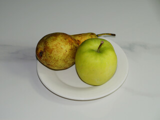 Green apple and pear on a white plate on the table