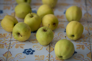 Organic yellow apples on colorful tiles, suitable for food branding, market advertising and seasonal produce visuals.