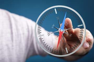 A person's finger points to a compass on a blue backdrop, symbolizing direction, navigation, and...