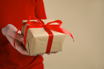 Woman with gift box on beige background, closeup. Space for text