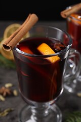 Tasty mulled wine in glass mugs, spices and fir branches on grey table, closeup