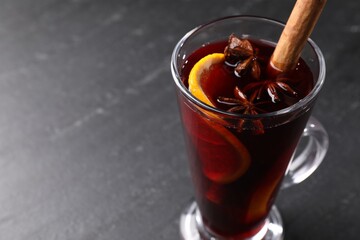 Tasty mulled wine in glass mug on black table, closeup. Space for text