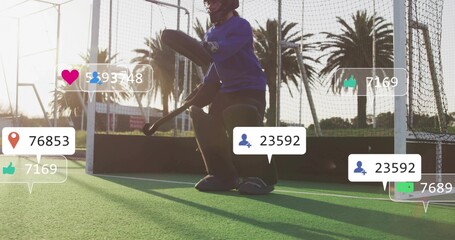 Crouching goalkeeper wearing full pads preparing to save at goal on fenced turf, social overlays