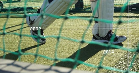 Framing batter's white batting pads and shoes through green netting on turf, showing 2002 2014