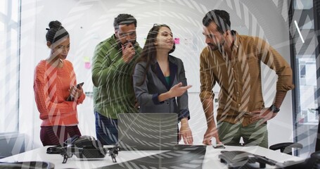 Presenting woman in dark blazer gesturing behind open laptop in meeting room with conference phones