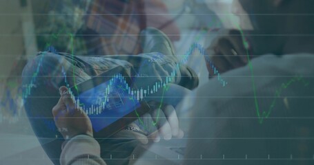 Holding man studying tablet in lounge wearing casual clothes with laptop and candlestick charts