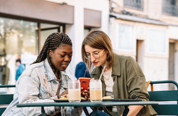Diverse women friends brunching and sharing smartphone