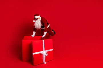Santa with a large red gift box on a bright red background ready for Christmas shopping and holiday season celebration