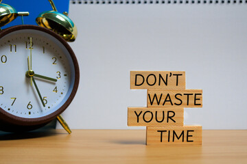 Wooden blocks with the words “DON’T WASTE YOUR TIME” placed near a classic clock,...