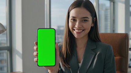 Close up of a confident woman in a modern office, holding a smartphone with a vibrant green screen. She smiles warmly, showcasing the device. - Powered by Adobe