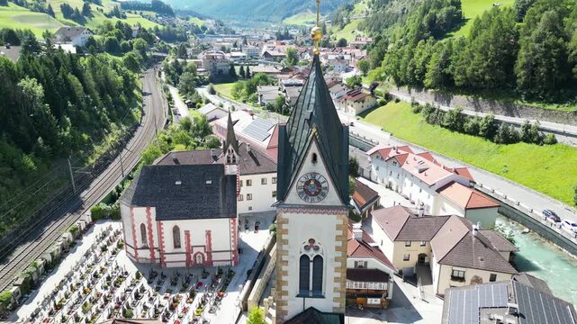 church steeple detail in austria near brenner pass scenic small town in the alps with mountain background river train tracks alpine village christian cross top colorful white drone footage scene 