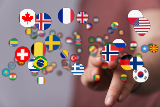 A hand reaches towards a collection of floating flag icons, symbolizing global connections, international relations, and cultural diversity. Per
