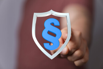 A person's hand holding a shield with the paragraph symbol inside. A concept of legal protection.