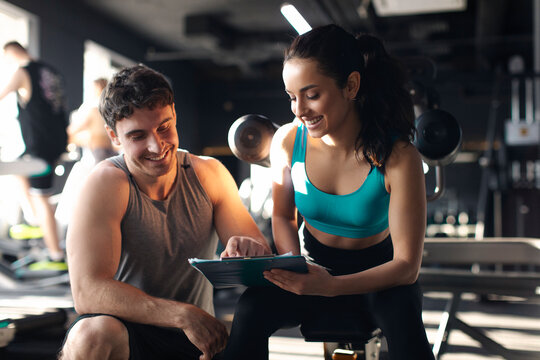 Man trainer and woman engaged in discussion in gym, reviewing plan of training, likely focusing on workout or nutrition plan