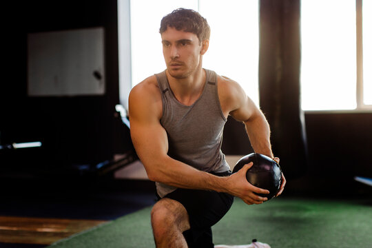 Strong focused man exercising with medicine ball, doing lunges in gym interior, guy having morning workout - Powered by Adobe