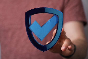 A person's hand holding a digital shield with a check mark, representing concepts of security,...