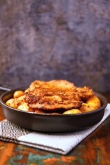 Fried pork steaks in a frying pan with potatoes. Rustic wooden background. Soft focus.	