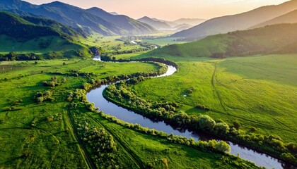 An aerial view captures a vibrant green valley with a winding river, rolling hills, and distant mountains bathed in the soft light of sunrise.