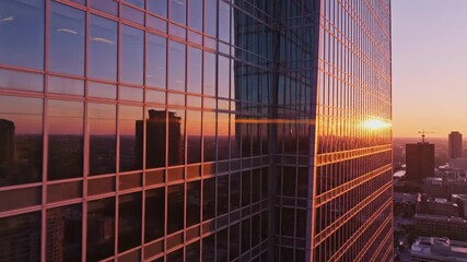 Aerial view of a glass skyscraper facade at sunset. The city skyline and golden sun reflect in the modern building's windows. Corporate architecture and urban development concept - Powered by Adobe
