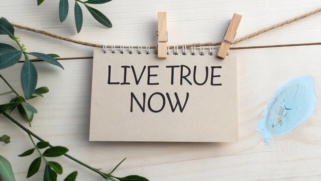 Live True Now: Inspirational Message on a Card Clipped to a String on a Light Wooden Background
