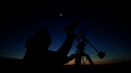 Fototapeta premium Amateur astro-photographer with a camera on a tripod photographing night sky with stars, planets, Moon and other celestial objects.