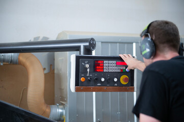 Ein Mann mit Geh&ouml;rschutz bedient eine digitale Steuerungseinheit einer Holzbearbeitungsmaschine in einer Werkstatt. Fokus auf das Display und die Technik, industrielle Umgebung.
