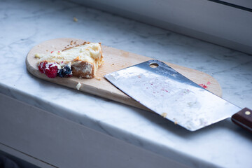 Angebrochene Beerentorte mit gro&szlig;em Messer auf Holzbrett in der K&uuml;che