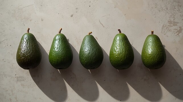 Five avocados aligned in a row on a light surface casting shadows in bright light conditions outdoors