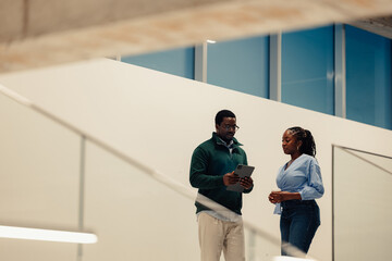 Coworkers discussing business holding tablet in modern office