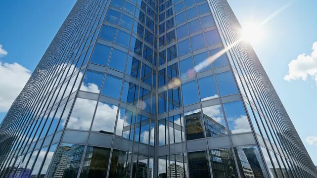 Vertical video zooming into a modern glass skyscraper in a city. Low angle view of a corporate office building with sky and cloud reflections. Business and finance concept