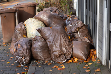 Garbage bags piled on sidewalk during autumn in a residential area