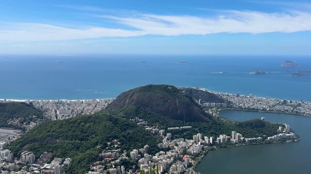Panoramic view of Rio de Janeiro from Corcovado, featuring Sugarloaf Mountain, Guanabara Bay, Santos Dumont Airport, and the Atlantic coastline under bright, partly cloudy weather.