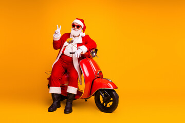 Santa on a red scooter in a bright yellow studio posing with a peace sign for a Christmas themed stock photo