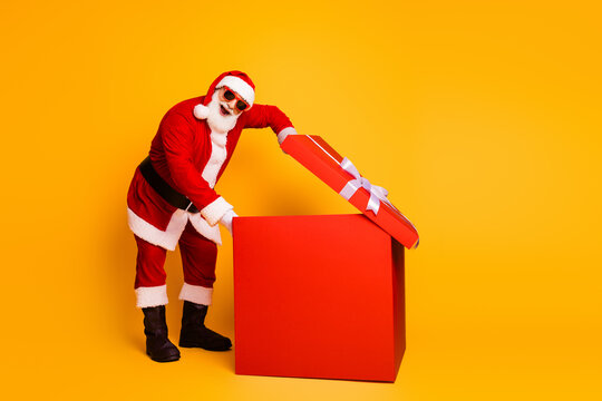 Happy Santa opens a large red gift box with white ribbon on a bright yellow backdrop for a festive christmas scene and holiday shopping - Powered by Adobe
