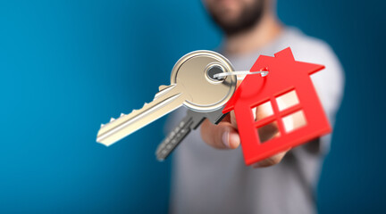 Close-up of a hand offering a house key with a red house-shaped tag, symbolizing homeownership and new beginnings. Perfect for real estate and m