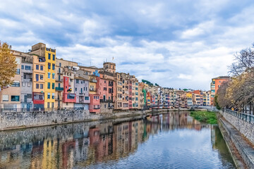 Colorful houses reflected in the Onyar River, Girona, Spain. A vibrant cityscape with a cloudy sky