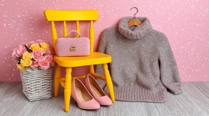 Stylish Women’s Outfit with Sweater, Heels, Handbag and Flowers on Yellow Chair against Pink Wall