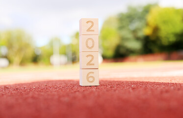 Colorful blocks showing the year 2026 stand on a park surface. The scene is bright and sunny, surrounded by greenery, perfect for welcoming the new year. Happiness fills the air
