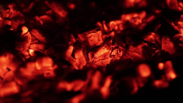 Hot, red burning embers from a bonfire glowing in the dark. A close-up view of smoldering charcoal creating a beautiful abstract background