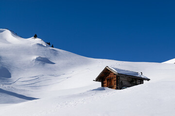 Wooden alpine cabin in snowy mountain landscape with ski tracks in the background under deep blue sky