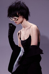 Stylish woman with short black hair wearing round glasses and a sleeveless black outfit in a...