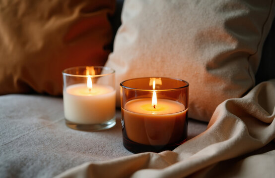 A cozy scene with lit candles placed on a soft surface near pillows creating a warm ambiance