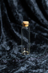 A small, tall, transparent glass bottle stands on a clean surface. It is completely empty, showcasing its slim shape and minimal design. 