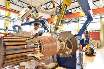 young mechanical engineering workers operate a machine for winding copper wire - manufacture of transformers in a factory