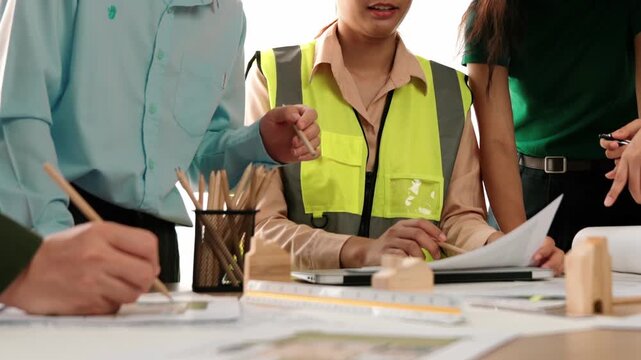 Smart architect and safety engineer discussion about building blueprint on table with architectural document, measurement tools and wooden block scatter around at modern office. Closeup. Delineation.