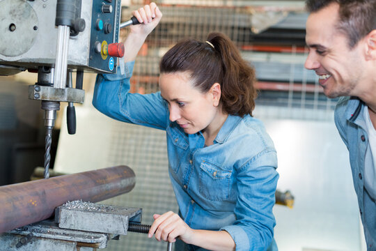 man supervising woman using bench drill