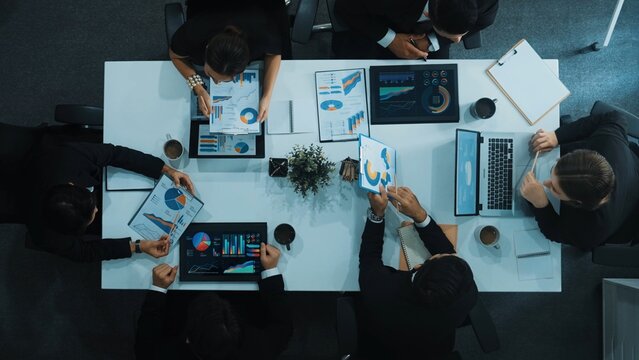 Top down aerial view of business people discussing about financial strategy on table with document and tablet display investment statistic at meeting. Diverse team brainstorm about plan. Directorate.