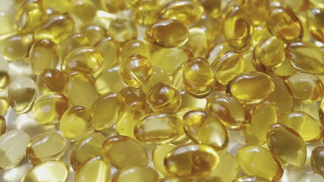 Top-down, close-up video of golden softgel capsules, like vitamin or fish oil supplements, slowly rotating on a turntable on white background showing concepts of healthcare, medicine, and nutrition.