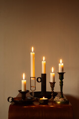 A warm still life of lit candles in vintage candleholders creating a cozy, atmospheric glow. Soft light and rustic textures enhance the intimate, timeless mood.