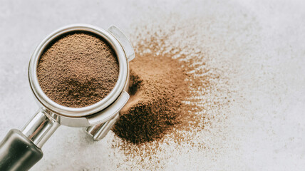 Ground coffee in a portafilter, ready for tamping. Preparation for espresso with spilled coffee powder creating a background texture